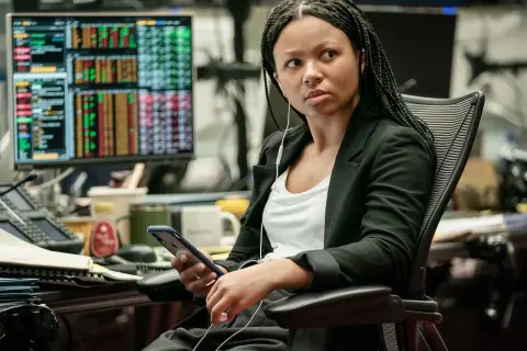 Myha'la Herrold, con auriculares, revisa su teléfono en una oficina con pantallas de datos financieros.
