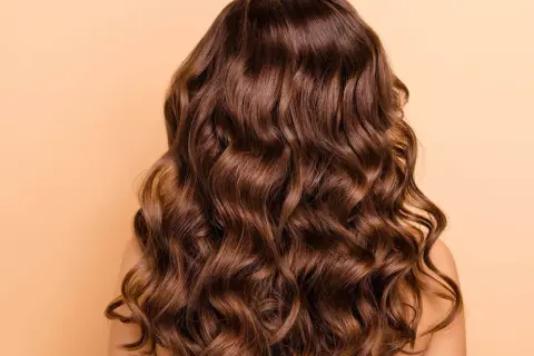 Cabello castaño con ondas naturales, un look de permanente ondulada que irradia brillo y movimiento.