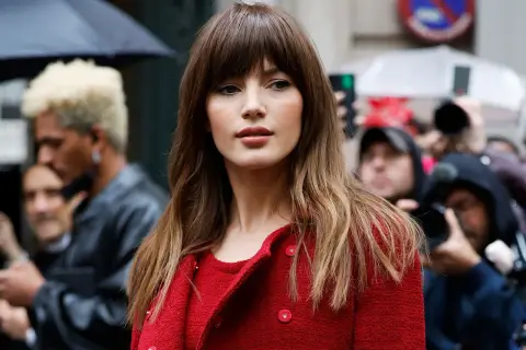 Mujer con flequillo y cabello castaño ondulado, luciendo un abrigo rojo. Un adelanto de los cortes de pelo 2026 mujer.
