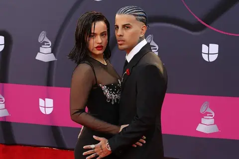 Rosalía y su novio, Rauw Alejandro, posan juntos en la alfombra roja. Ella luce un vestido negro con transparencias y pedrería, él un traje elegante.