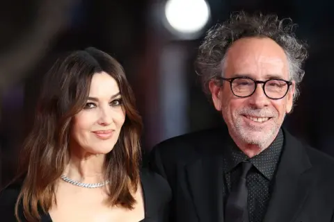 Monica Bellucci y Tim Burton, una pareja que parece sacada de una película de fantasía gótica, posan juntos con elegancia.