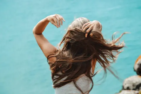 Mujer con cabello largo y castaño, con algunas canas visibles, moviendo su pelo al viento. Una alternativa natural para cubrir canas sin tinte.