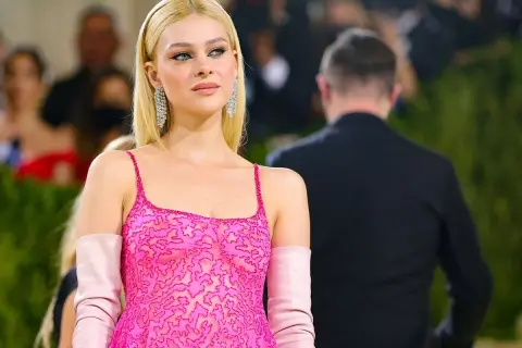 Nicola Peltz deslumbra con un vestido rosa vibrante y guantes a juego, luciendo elegante y radiante.