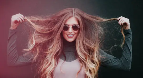 Chica sonriente con pelo largo y ondulado, mostrando cómo hidratar el pelo para un brillo radiante.