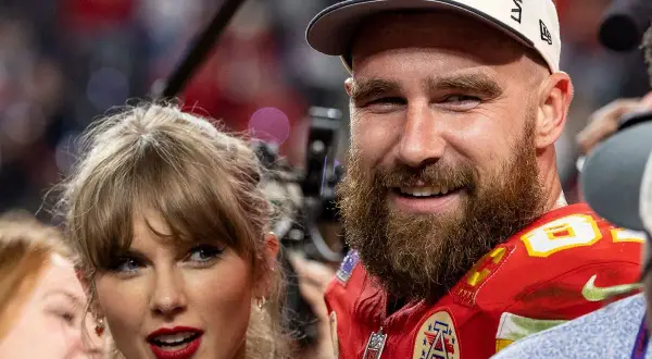 Travis Kelce, con gorra de campeones, sonríe junto a Taylor Swift, celebrando un momento especial.
