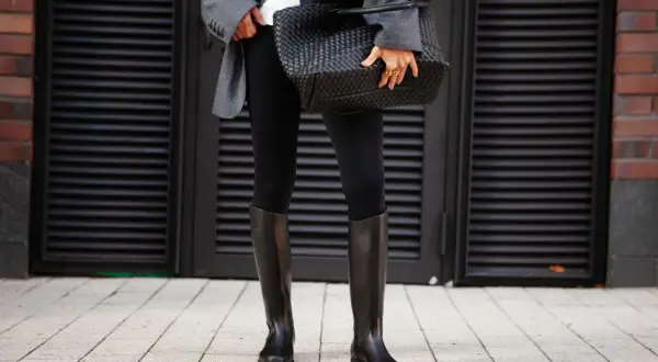 Elegante outfit con botas altas negras, chaqueta gris y bolso tejido.