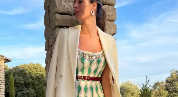 María de la Orden, con un vestido estampado y blazer blanco, posa junto a una pared de piedra bajo un cielo azul.