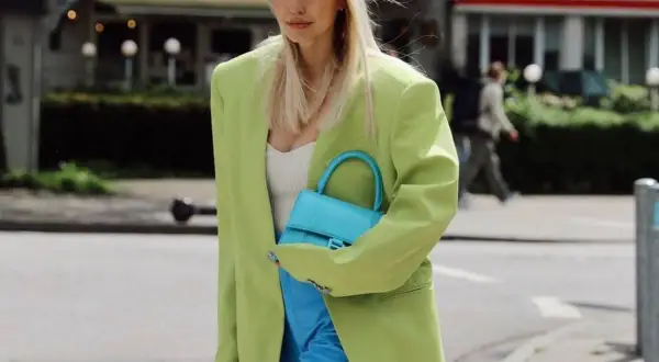 Mujer con blazer verde lima y pantalones azul eléctrico. Su bolso turquesa complementa perfectamente el conjunto, demostrando cómo el **verde y azul combinan** a la perfección.