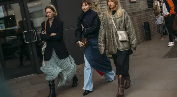 Tres mujeres caminan, mostrando que zapatos se llevan este invierno: botas altas negras, botines marrones y zapatos negros.