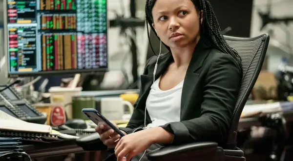 Myha'la Herrold, con auriculares, revisa su teléfono en una oficina con pantallas de datos financieros.