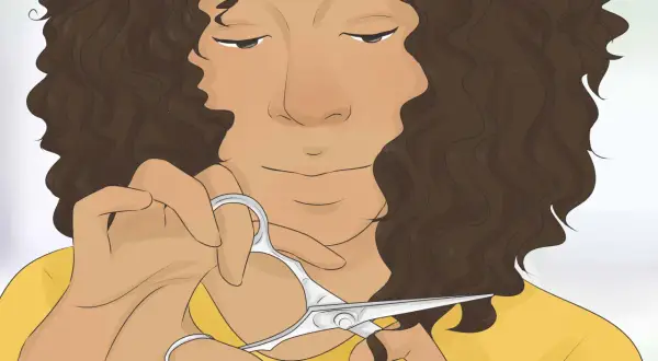 Mujer con cabello castaño rizado a capas, cortándose el pelo con tijeras.