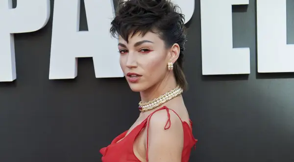 Mujer con un llamativo mullet corto, maquillaje rojo y vestido rojo, luciendo un collar de perlas.