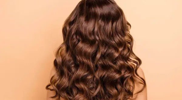 Cabello castaño con ondas naturales, un look de permanente ondulada que irradia brillo y movimiento.