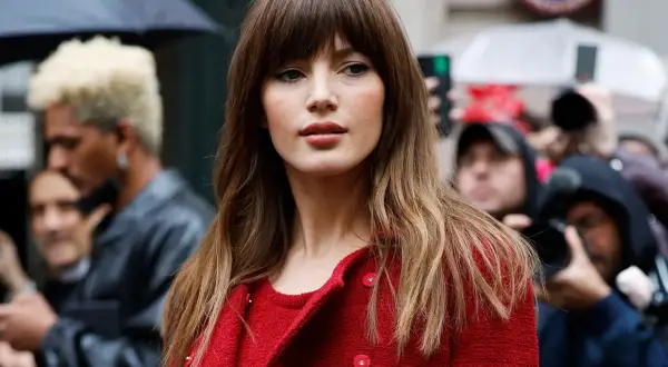 Mujer con flequillo y cabello castaño ondulado, luciendo un abrigo rojo. Un adelanto de los cortes de pelo 2026 mujer.