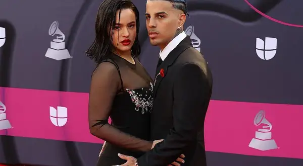 Rosalía y su novio, Rauw Alejandro, posan juntos en la alfombra roja. Ella luce un vestido negro con transparencias y pedrería, él un traje elegante.