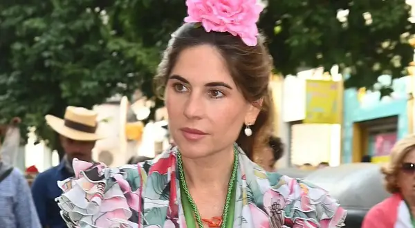 Lourdes Montes luce un vestido floral con volantes y una gran flor rosa en el pelo, adornada con un collar verde.