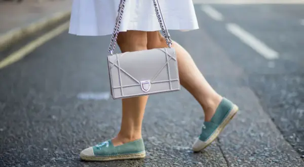 Piernas con un outfit veraniego, falda blanca y un bolso gris, completado con unas cómodas alpargatas de tela azul.