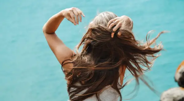 Mujer con cabello largo y castaño, con algunas canas visibles, moviendo su pelo al viento. Una alternativa natural para cubrir canas sin tinte.