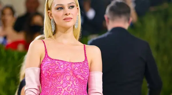 Nicola Peltz deslumbra con un vestido rosa vibrante y guantes a juego, luciendo elegante y radiante.