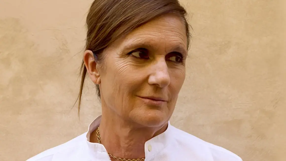 Retrato de Maria Grazia Chiuri, diseñadora de moda, con un collar dorado y camisa blanca.