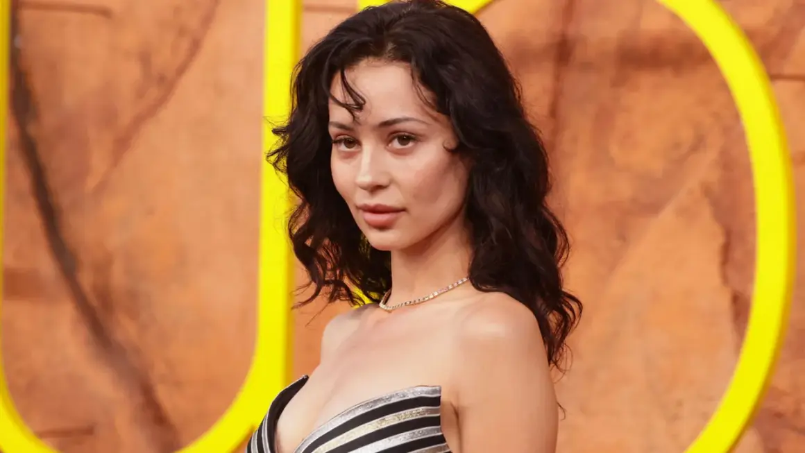 Alexa Demie, con cabello oscuro y ondulado, luce un collar de diamantes y un vestido a rayas.