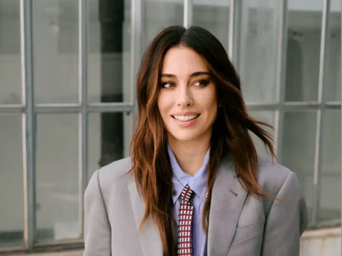 Blanca Suárez, con su melena castaña al viento, sonríe con confianza luciendo un traje gris y corbata.