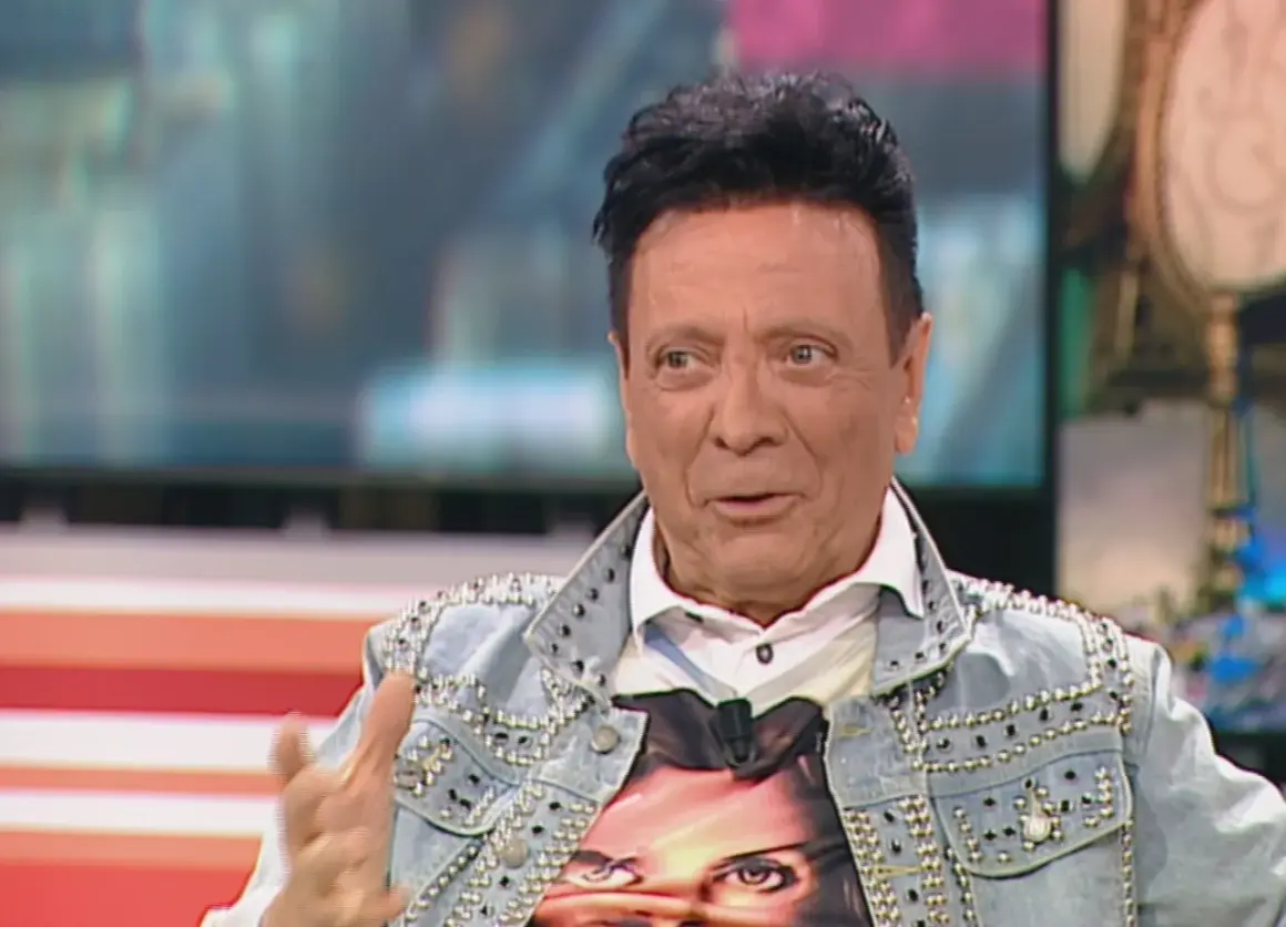 Rupert, el peluquero, luce una chaqueta vaquera tachonada y una camiseta con un rostro.