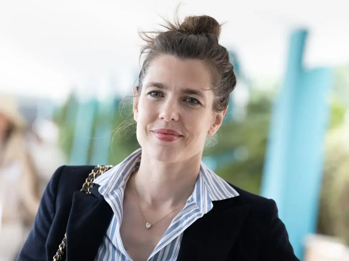 Carlota Casiraghi sonríe con su cabello recogido en un moño, luciendo un blazer oscuro y un collar con un colgante en forma de corazón.