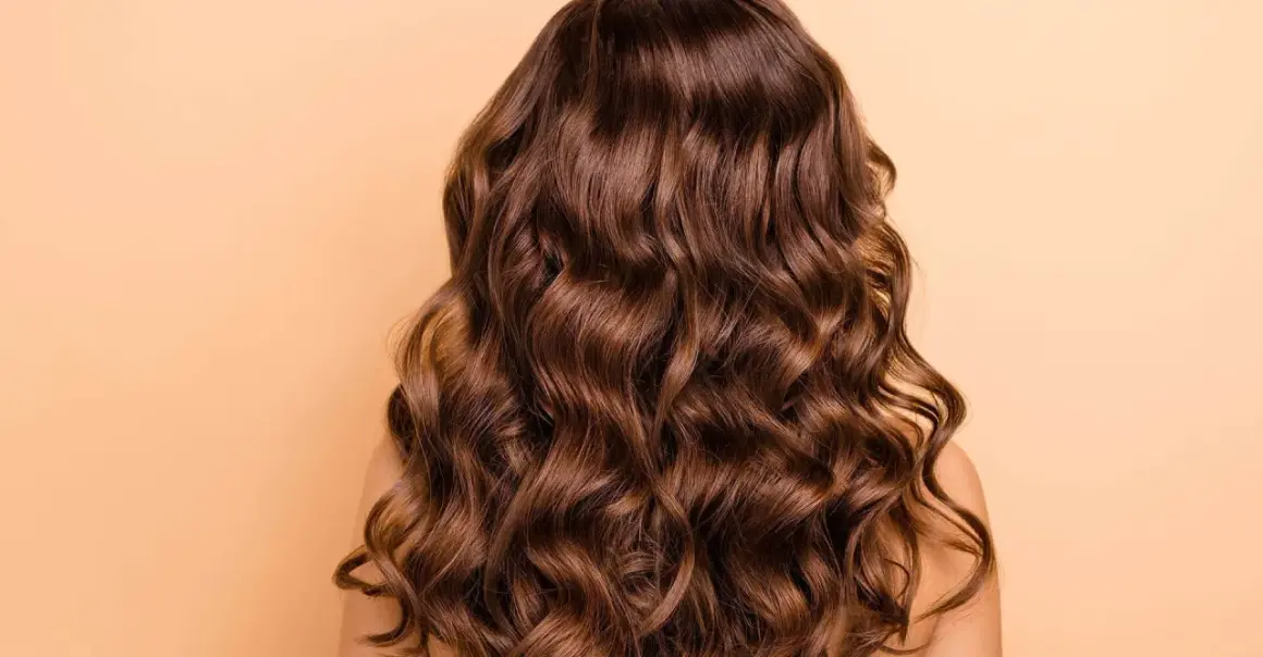 Cabello castaño con ondas naturales, un look de permanente ondulada que irradia brillo y movimiento.