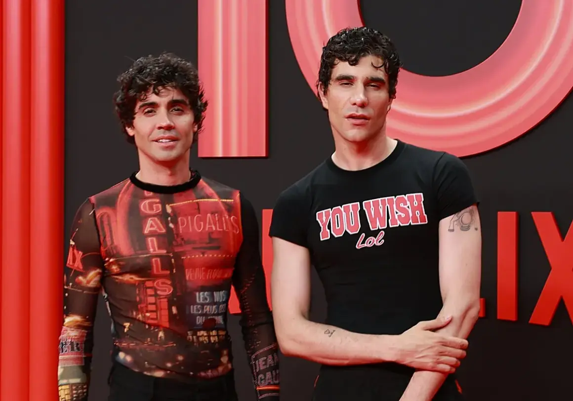 Javier Calvo y Javier Ambrossi posan sonrientes. Javier Calvo lleva una camiseta con estampado de luces de neón y Javier Ambrossi una camiseta negra con el lema "You Wish Lol".