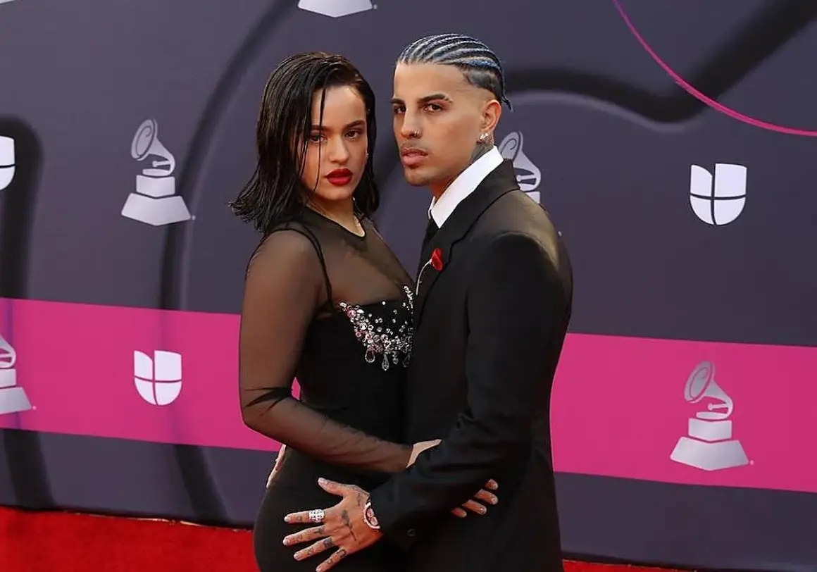 Rosalía y su novio, Rauw Alejandro, posan juntos en la alfombra roja. Ella luce un vestido negro con transparencias y pedrería, él un traje elegante.