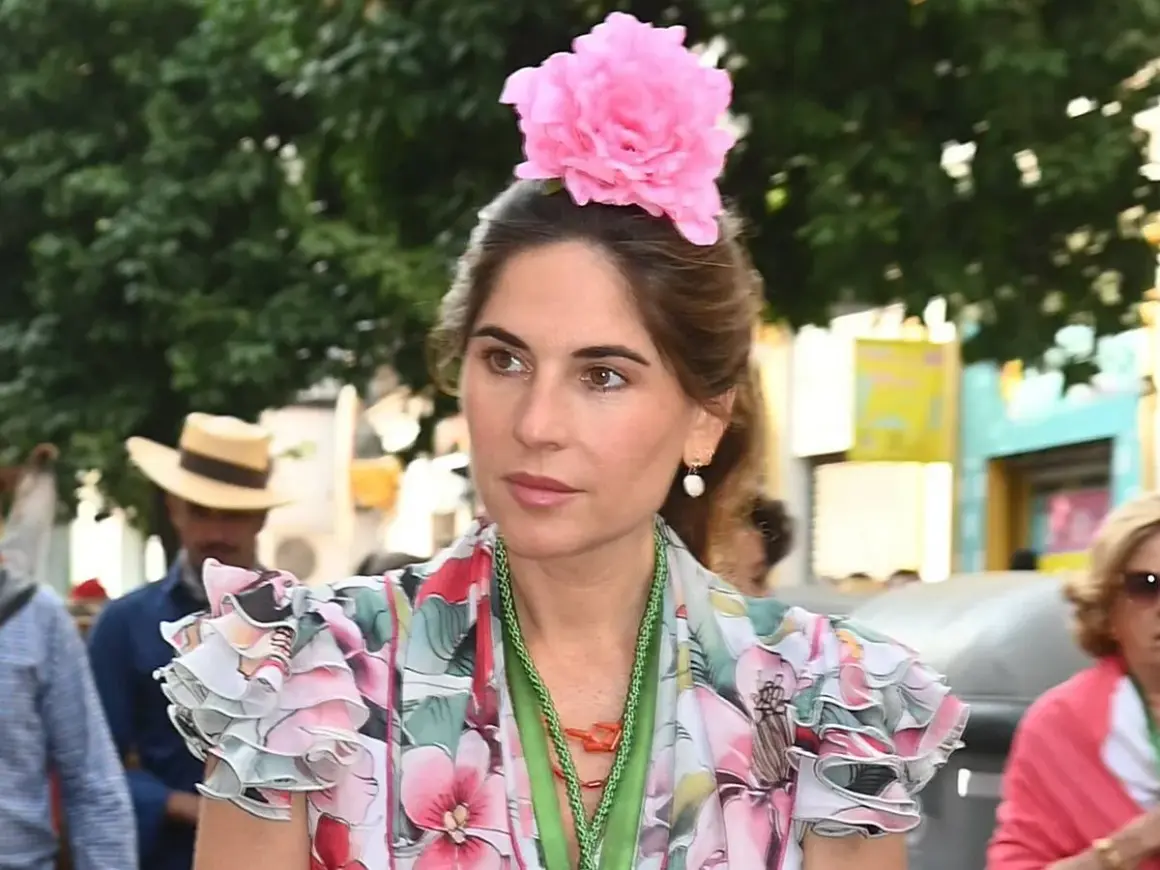Lourdes Montes luce un vestido floral con volantes y una gran flor rosa en el pelo, adornada con un collar verde.
