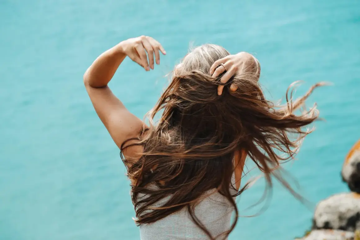 Mujer con cabello largo y castaño, con algunas canas visibles, moviendo su pelo al viento. Una alternativa natural para cubrir canas sin tinte.