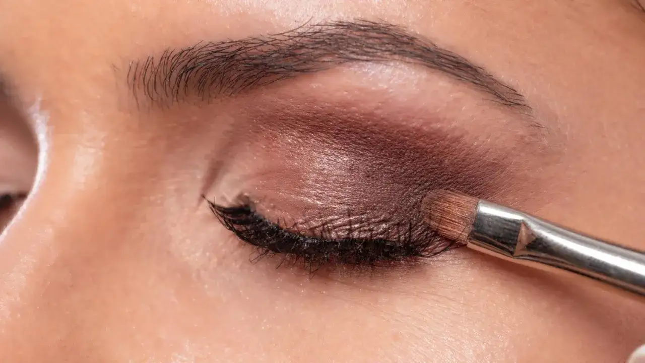 Aplicando sombra de ojos marrón con brocha. Descubre cómo maquillar los ojos a partir de los 50 años para un look radiante.