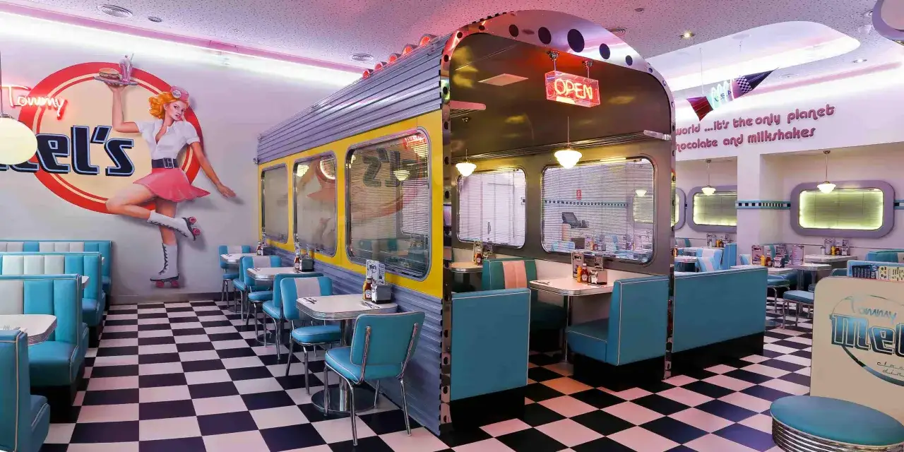 Interior de un diner estilo años 50, con mesas, asientos turquesa y un mural de 