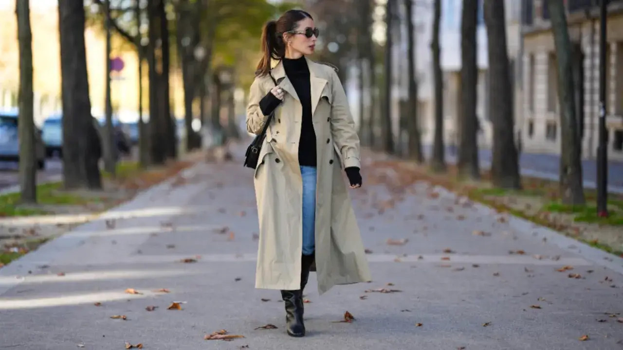 Mujer pasea con estilo, luciendo un trench beige, jersey negro y vaqueros. Un look perfecto para como vestir en oto&ntilde;o en Espa&ntilde;a.