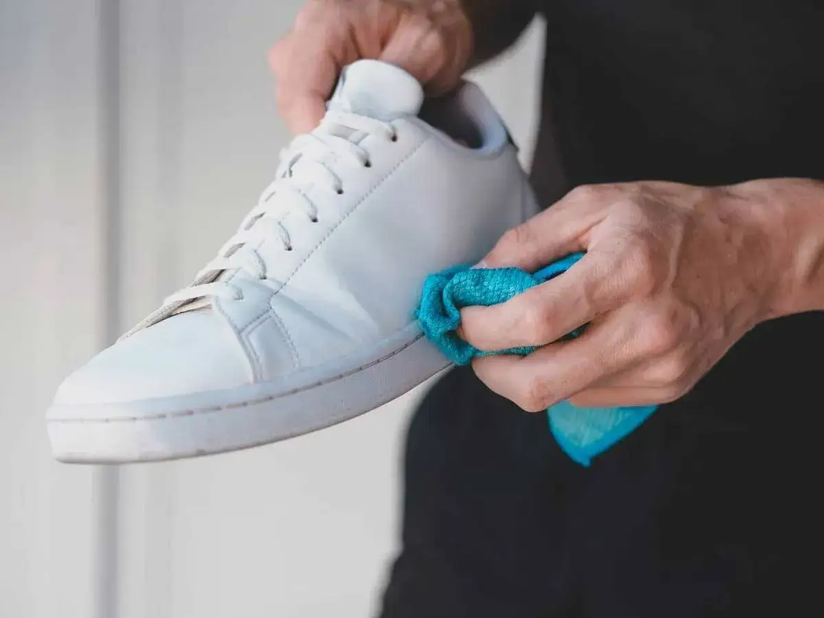Man limpiando zapatillas blancas piel con un paño azul.