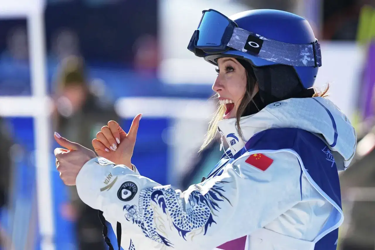 Eileen Gu, con casco azul y gafas, sonríe y hace un gesto de 