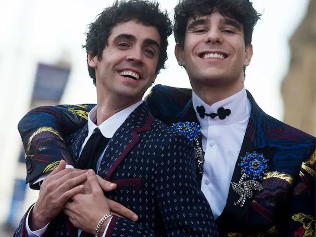 Javier Calvo y Javier Ambrossi, sonrientes y abrazados, lucen trajes llamativos con broches azules.
