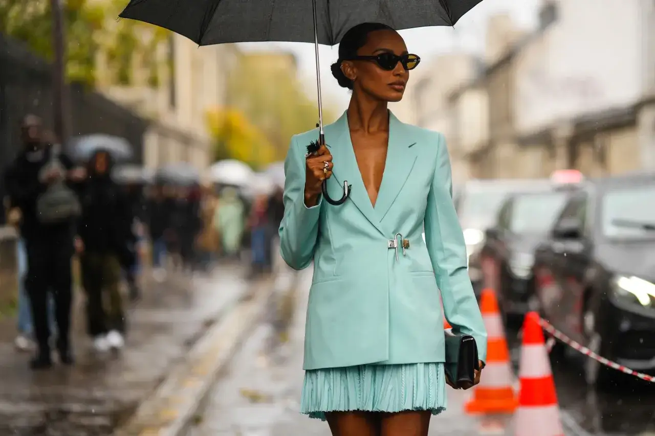 Mujer con un elegante outfit de lluvia color menta, sosteniendo un paraguas negro y gafas de sol.