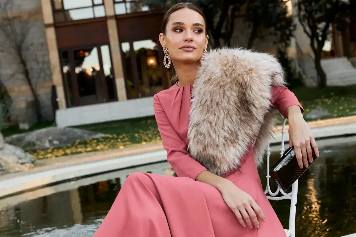 Elegante vestido rosa para una boda en invierno, con un chal de pelo y un bolso de mano.
