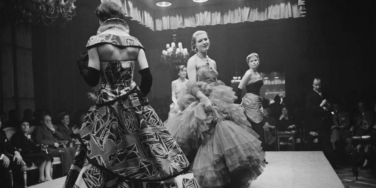 Desfile de alta costura, un momento clave en la historia de la moda. Modelos lucen vestidos voluminosos y estampados audaces ante un público atento.