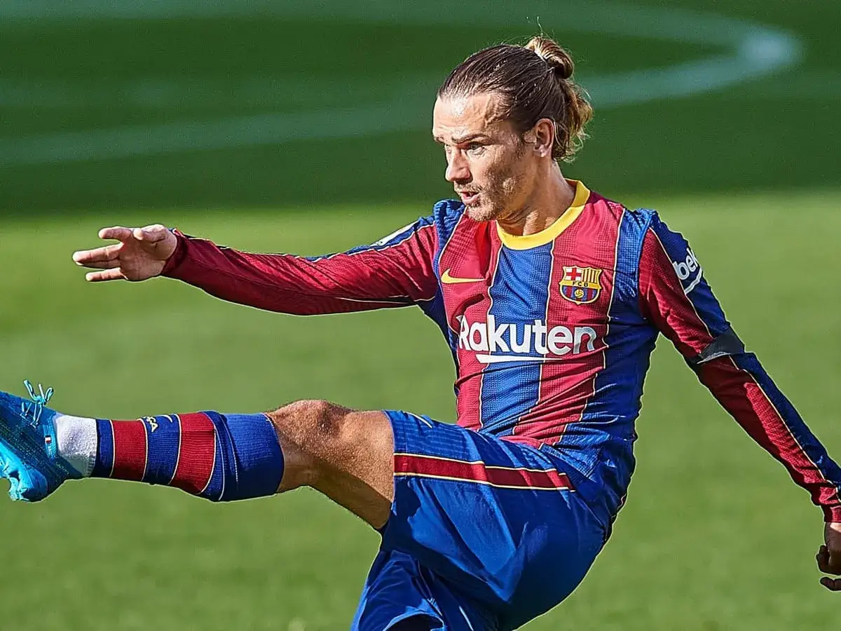 Antoine Griezmann, con su icónico moño, patea el balón con fuerza en un partido.