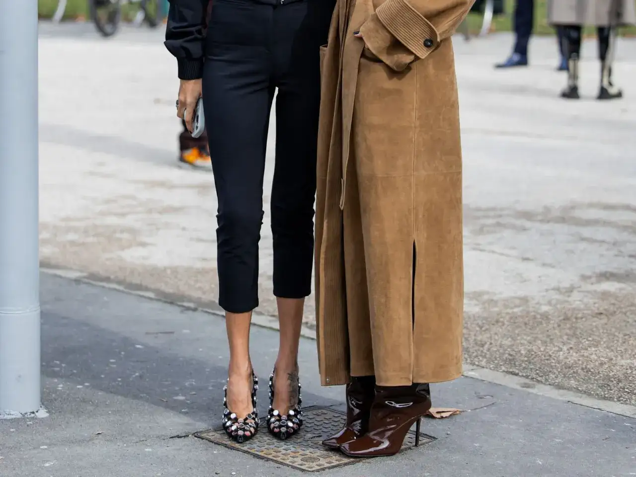 Dos mujeres muestran que zapatos se llevan este invierno: unos tacones joya y unas botas de charol.