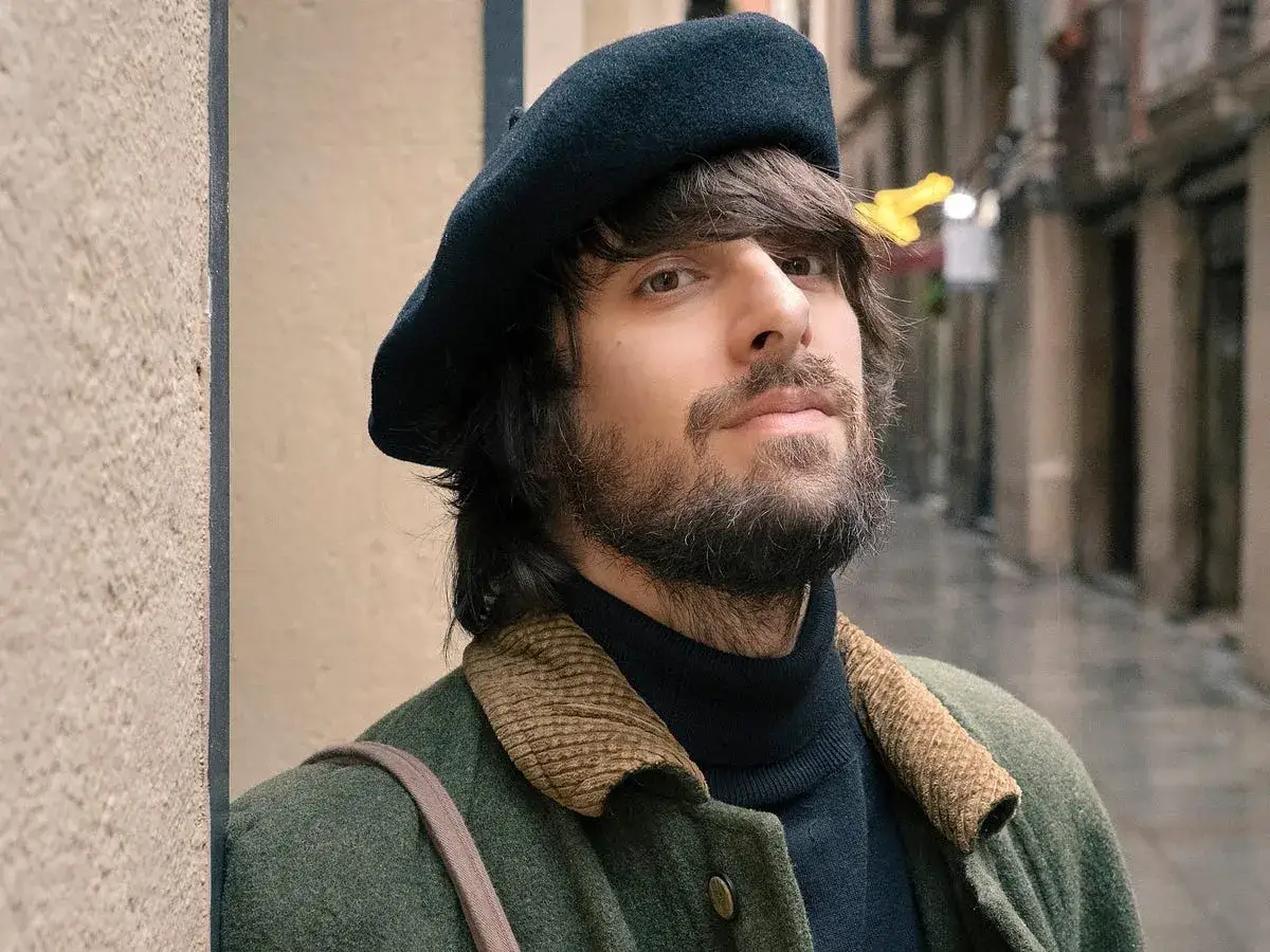 David Ucles, con boina y abrigo verde, posa en una calle adoquinada.