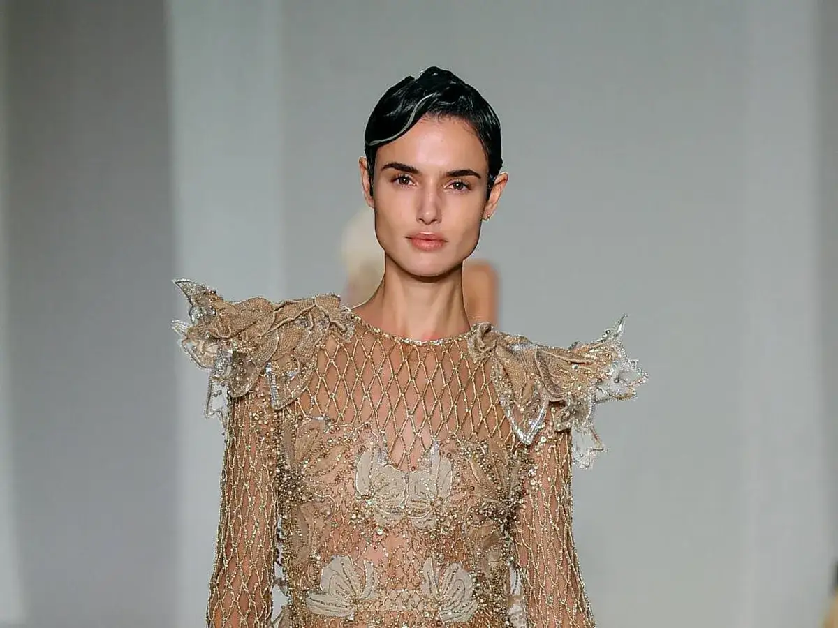 Belen Corsini desfila con un vestido dorado de pedrería y volantes en los hombros, un diseño que evoca la elegancia de la alta costura.