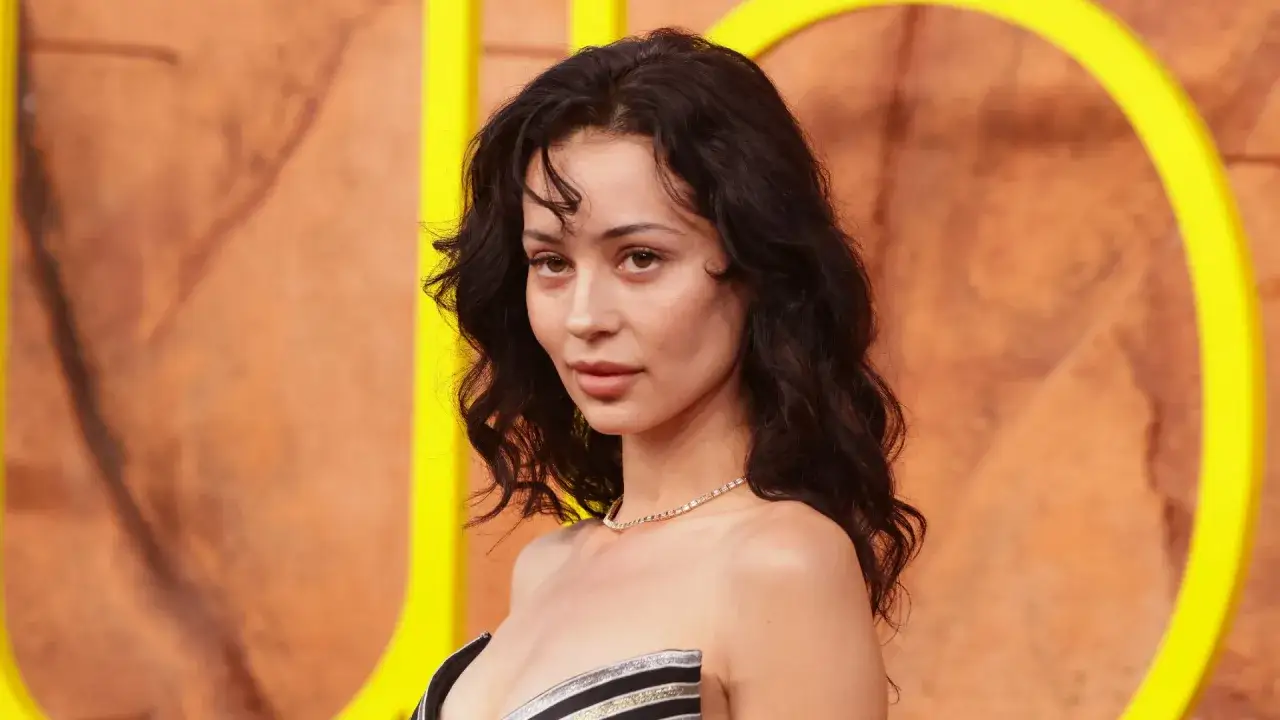 Alexa Demie, con su cabello oscuro y ondulado, luce un collar de diamantes y un vestido a rayas.