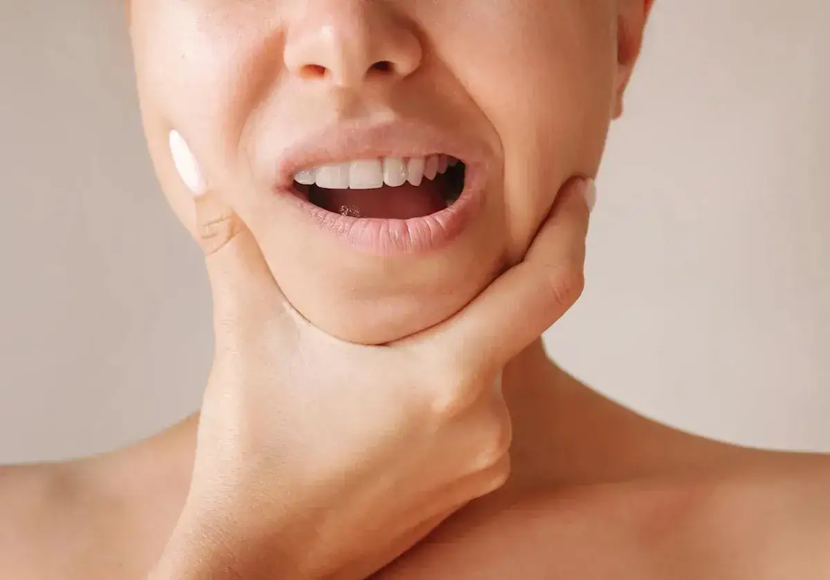 Una mano presiona la mejilla de una persona, mostrando la boca abierta y los dientes. ¿Es esto parte de la técnica de mewing?