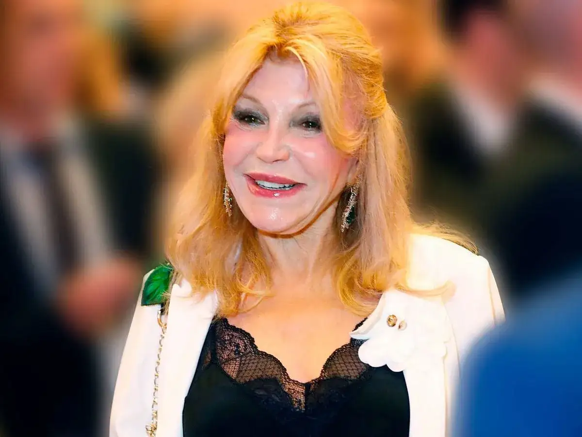Tita Thyssen sonríe con elegancia, luciendo un blazer blanco sobre un top de encaje negro.