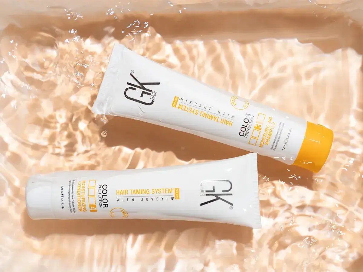 Dos tubos de GK Hair, uno de champú y otro de acondicionador, flotan en agua clara. Descubre cómo hidratar el pelo con estos productos.